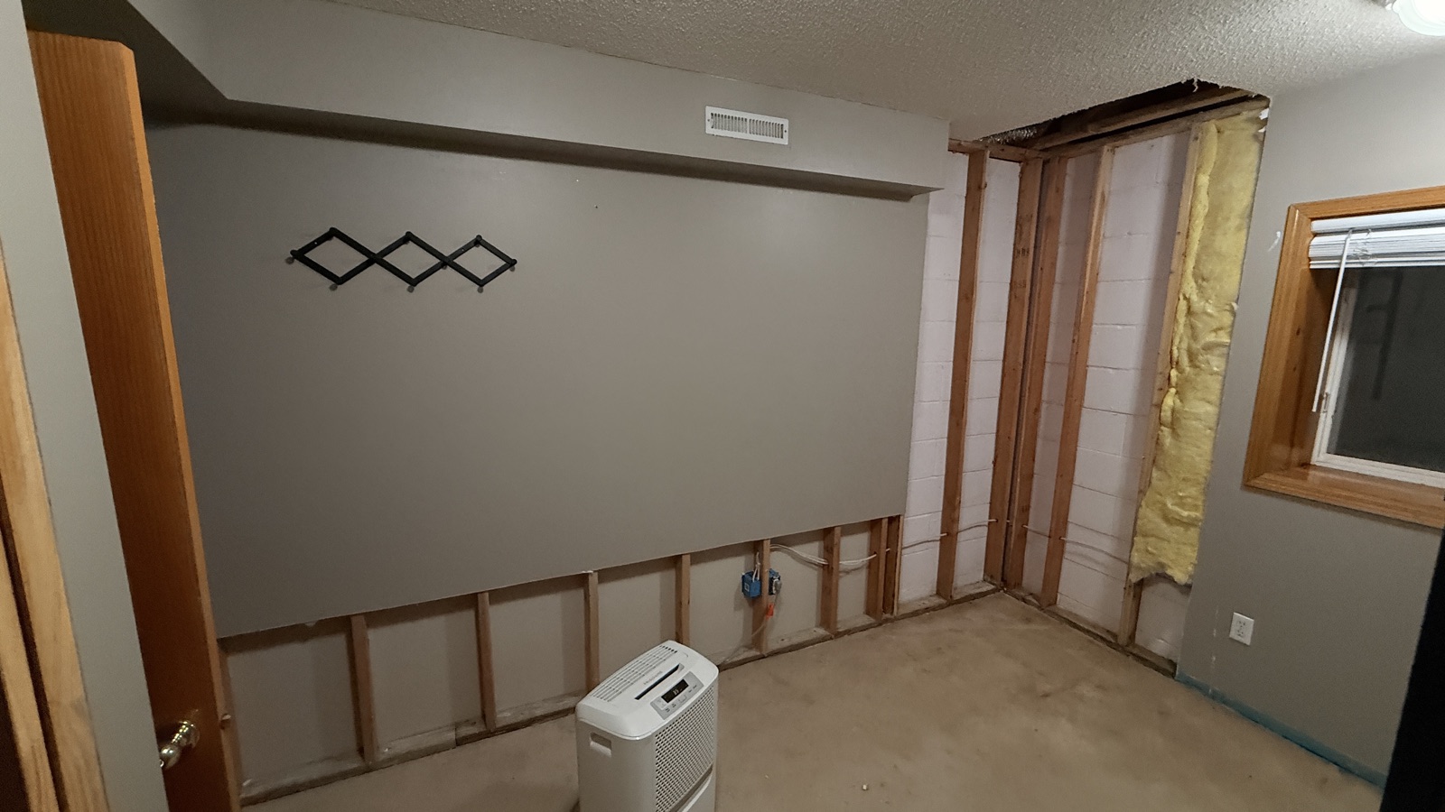 Water-damaged basement wall opened to the block with a dehumidifier running